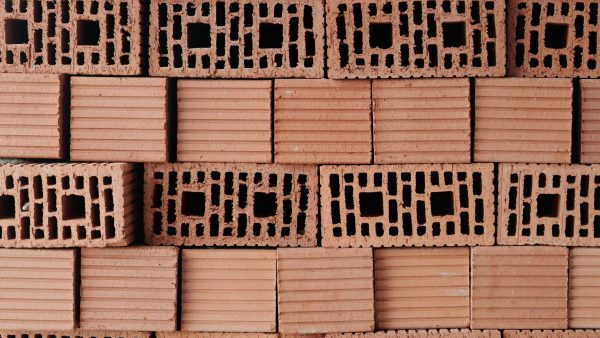 Stack of red solid clay bricks formed by several layers prepared for building work while making background or wallpaper