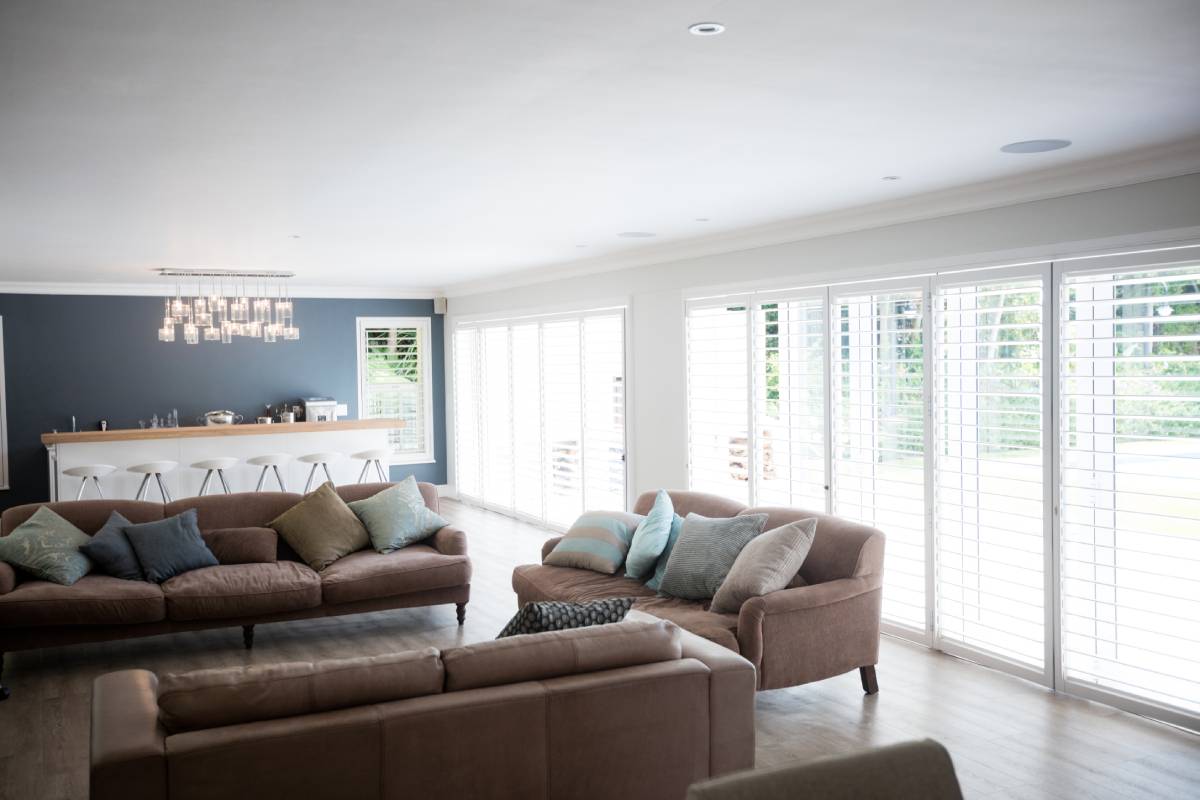 Large white Hamptons style plantation shutters in a luxury living room with dark wood flooring.